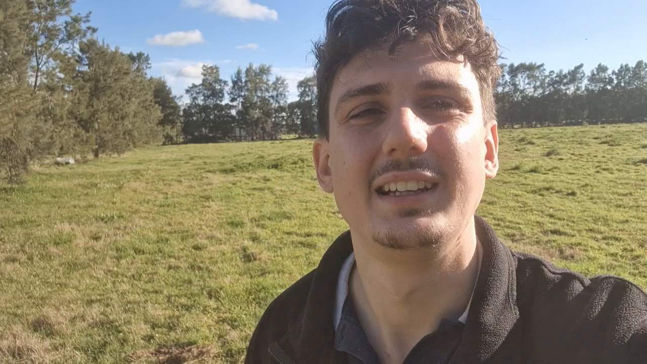 Stanley Kunz erzählt auf einer Weide in Uruguay in die Kamera, hinter ihm hohe Bäume.