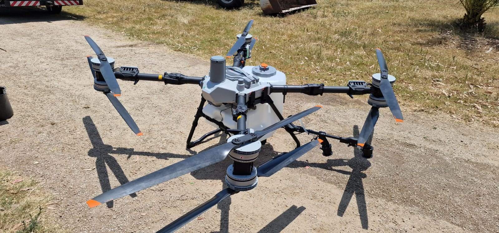 Eine große Agrardrohne mit ausgeklappten Rotorarmen steht auf einem Schotterplatz.